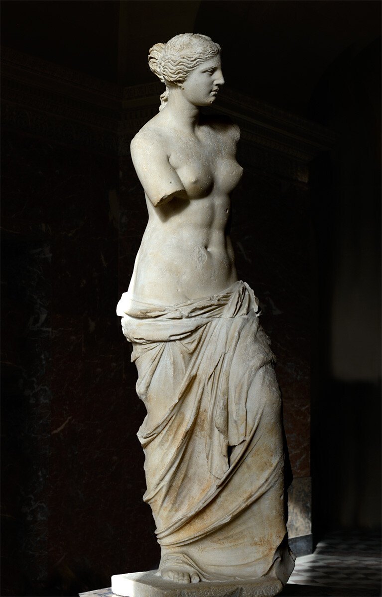 Marble statue of an armless draped female figure in a dark museum room
