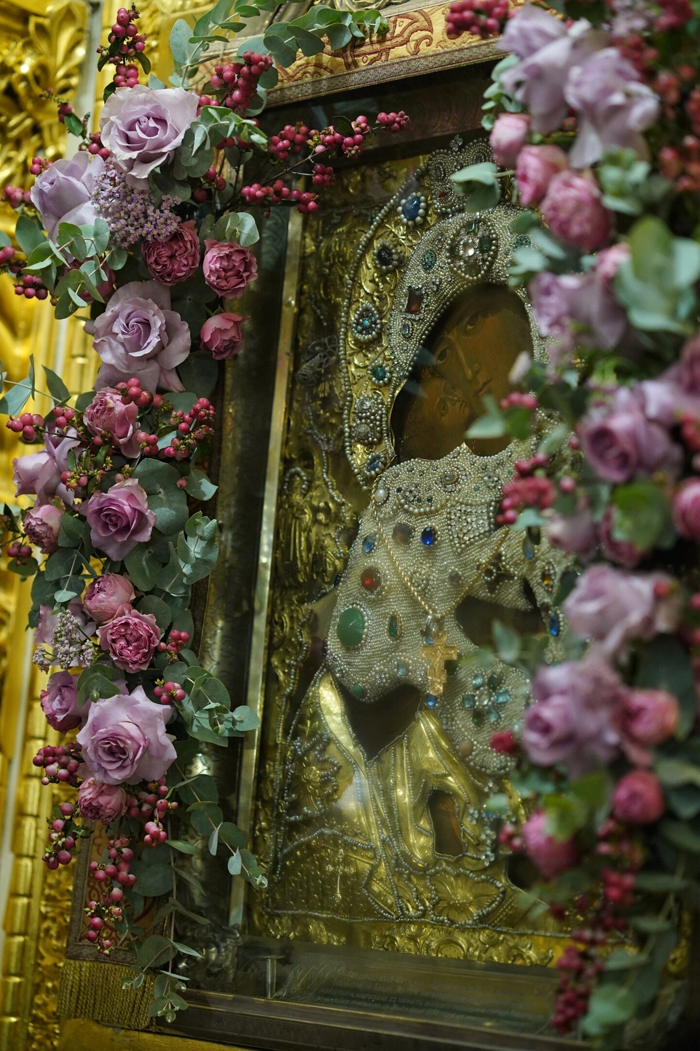 Golden icon framed with garlands of pink roses and red berries
