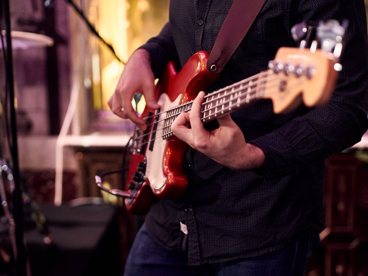 Close-up of hands playing a red bass guitar on a dimly lit stage