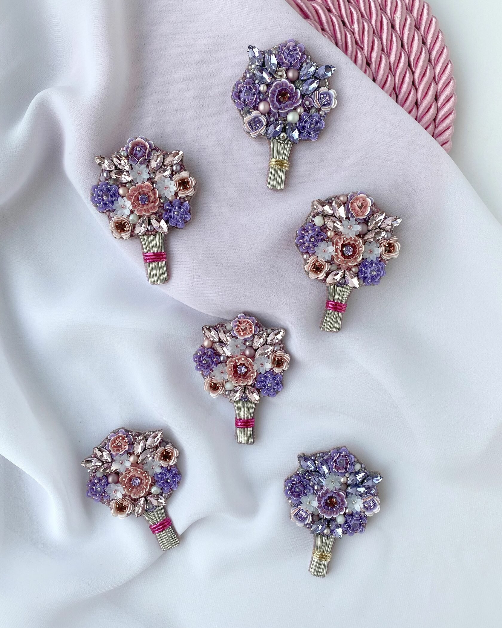 Six beaded flower bouquet brooches in purple and pink on white fabric