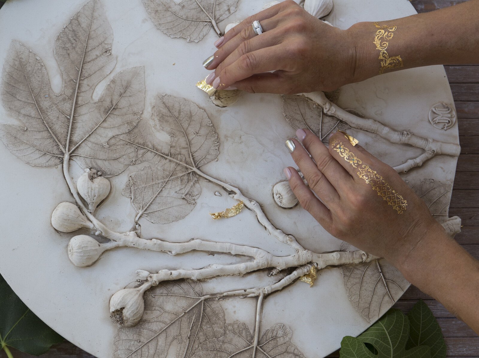 Hands applying gold leaf to a fig branch and leaf plaster relief