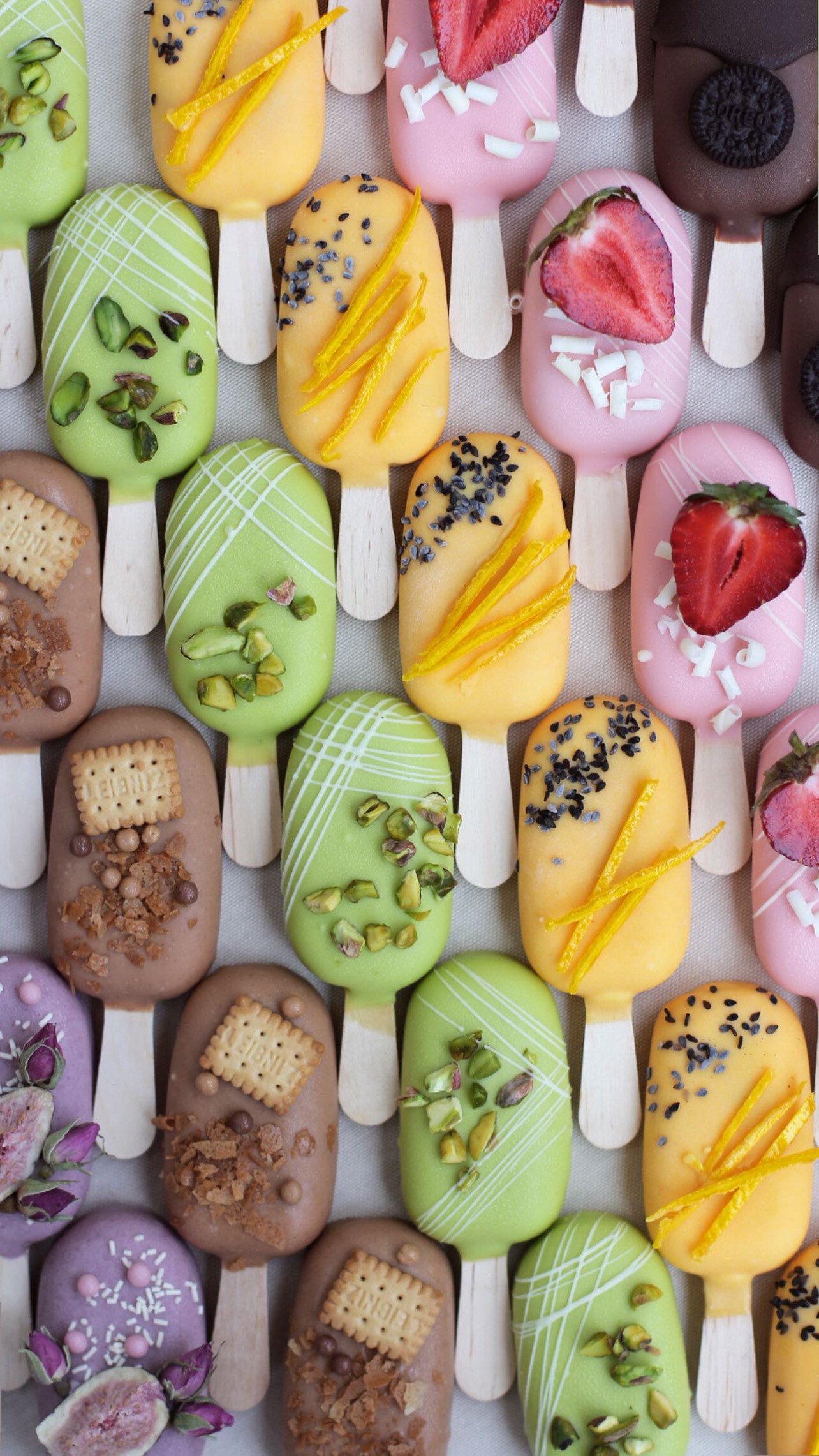 Colourful glazed desserts on sticks decorated with pistachios, strawberries and citrus zest