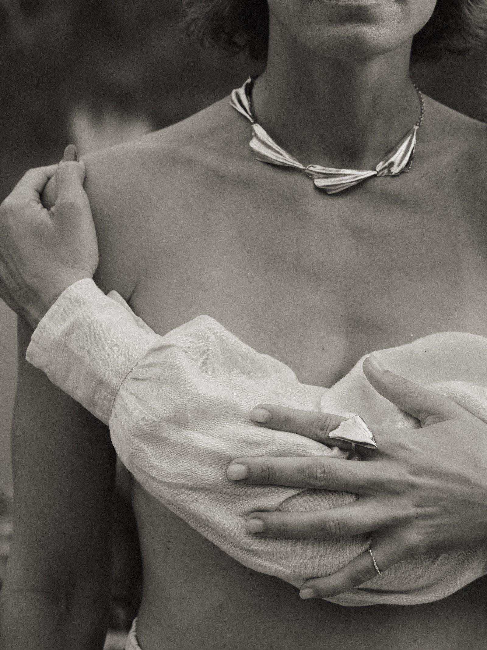 Black and white close-up of a woman's torso with a silver necklace and linen sleeve