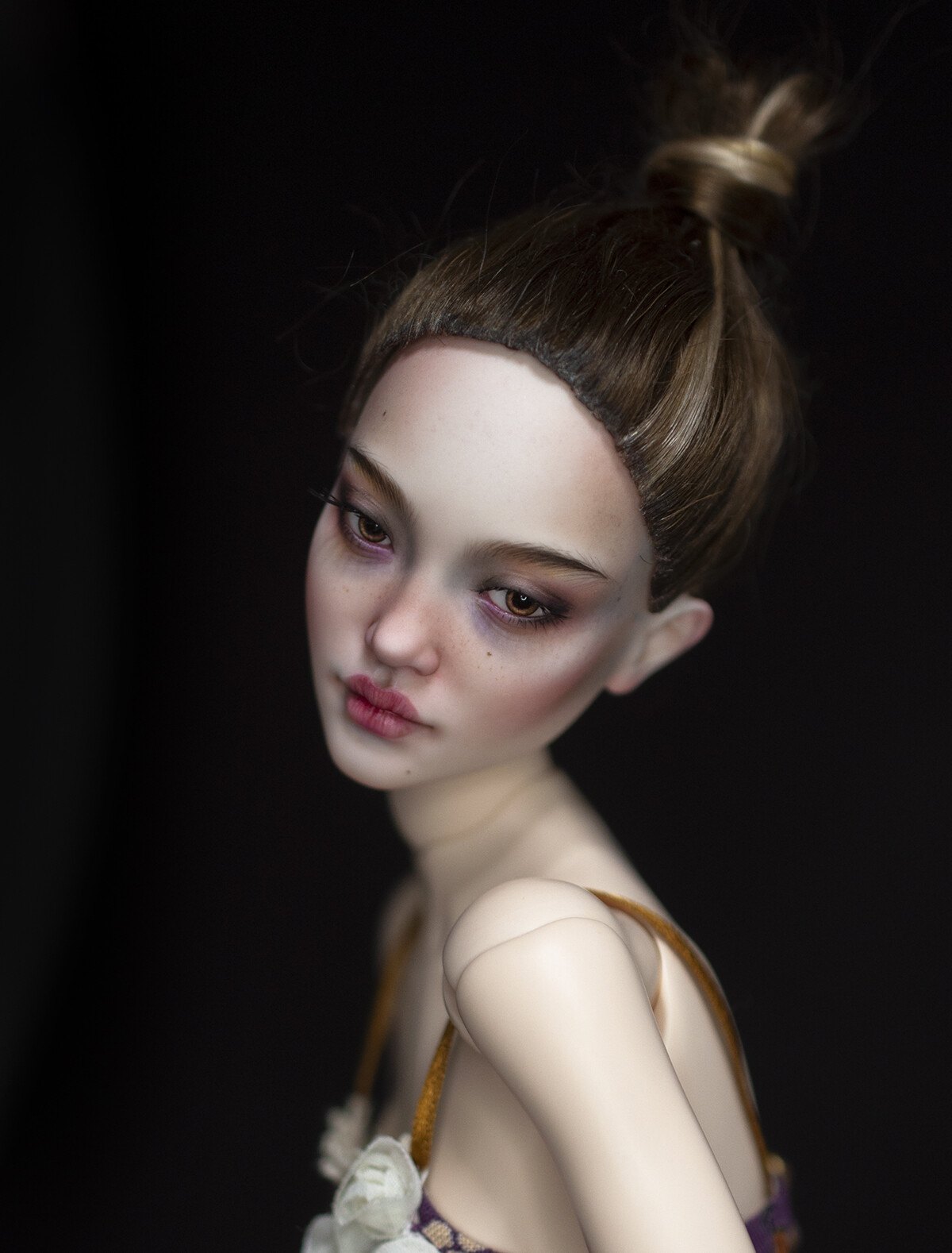Art doll with hair in a top bun and purple eyeshadow on a dark background