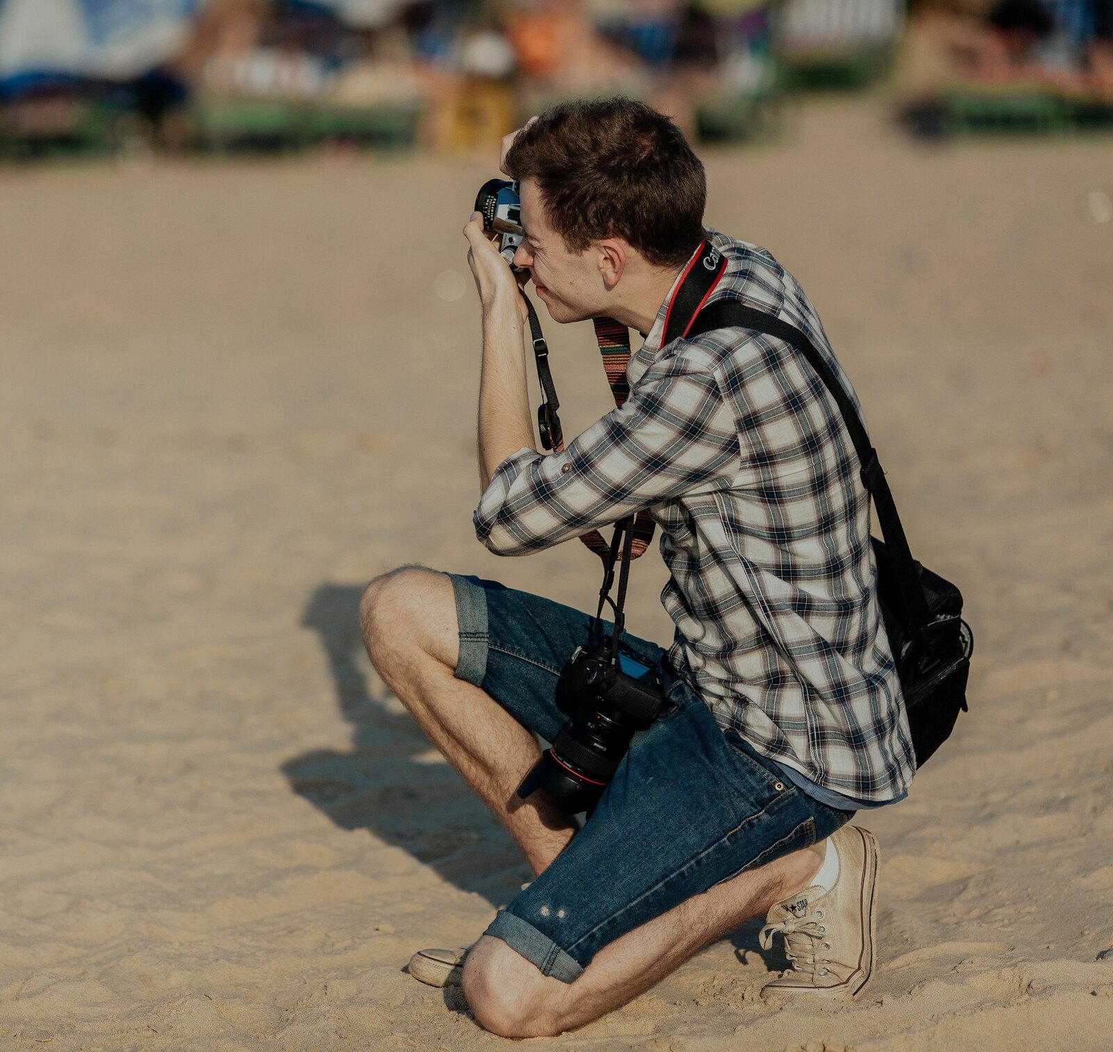 Young man crouching on a sandy beach taking a photograph with a camera