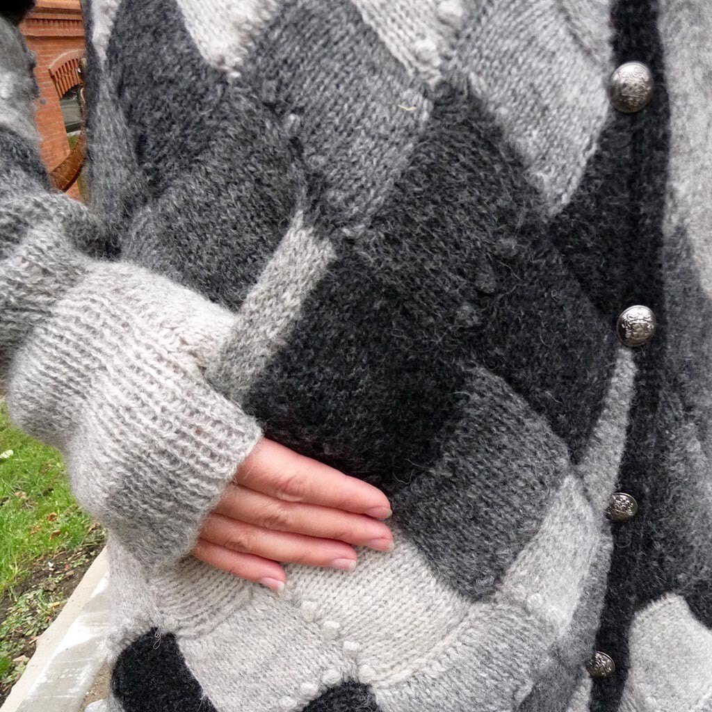 A hand resting on a grey entrelac knitted cardigan with metal buttons
