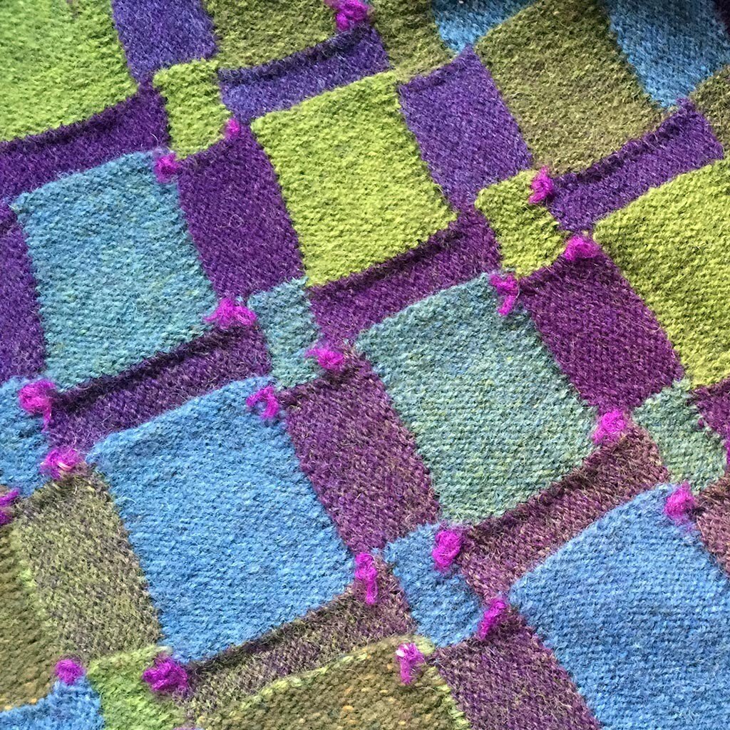 Colourful entrelac knitted fabric in purple, green and blue with magenta tufts