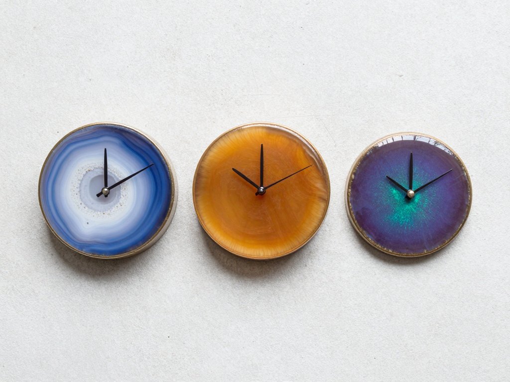 Three round resin clock bodies in agate, amber and chameleon finishes on concrete