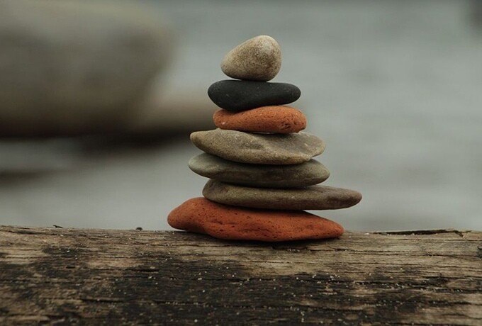 Stack of balanced smooth stones in gray and orange on a weathered wooden log