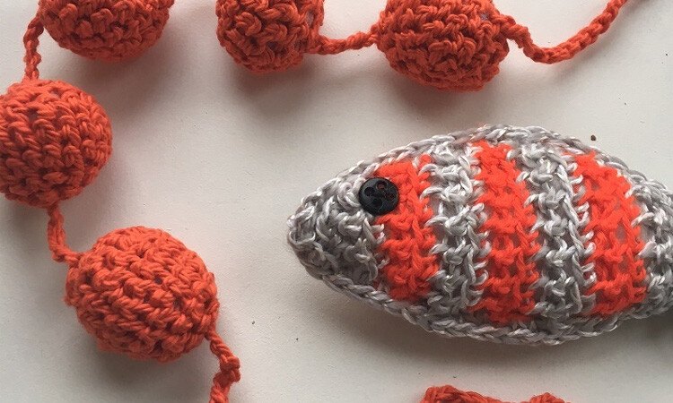 Crocheted gray and orange fish toy beside linked orange yarn balls