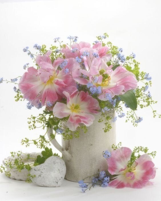 Bouquet of pink tulips and blue forget-me-nots in a white jug beside a stone heart