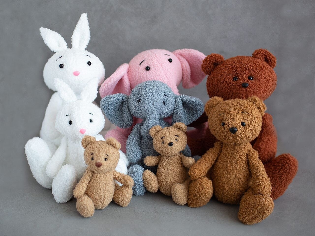 Group of handmade plush bunnies, elephants and teddy bears against a gray background