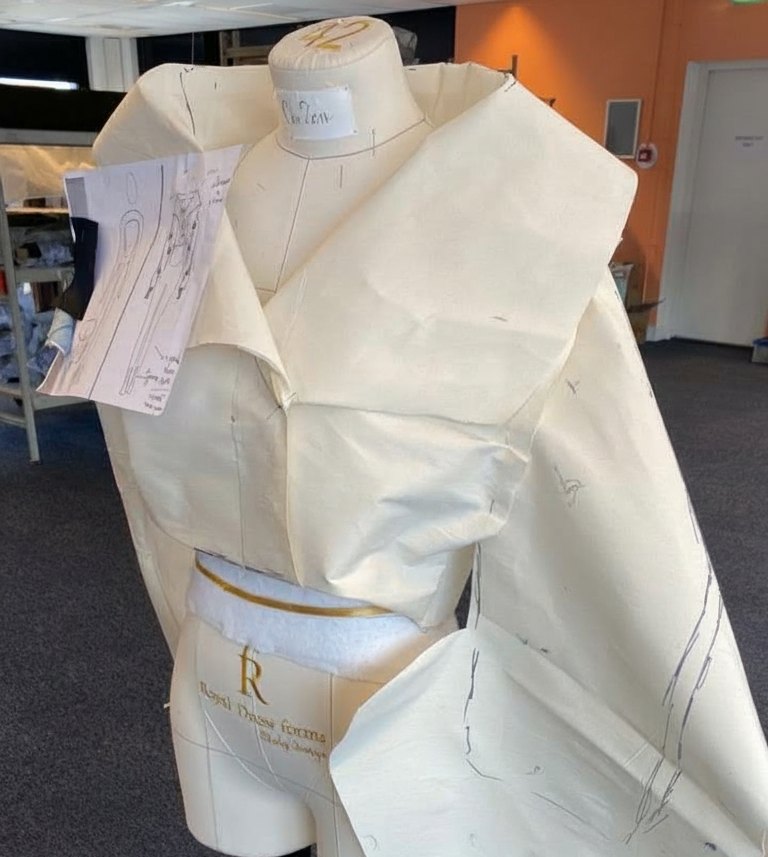 A dress form with a draped muslin collar and attached sketch