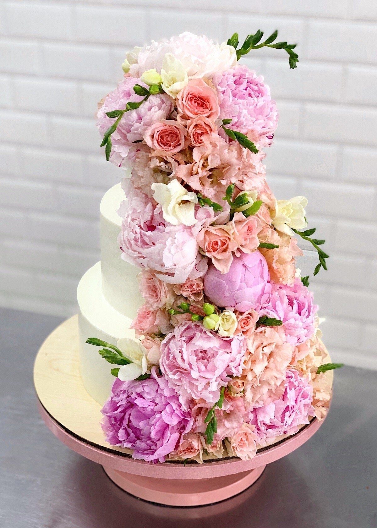 Two-tier white cake decorated with pink flowers on a pink stand