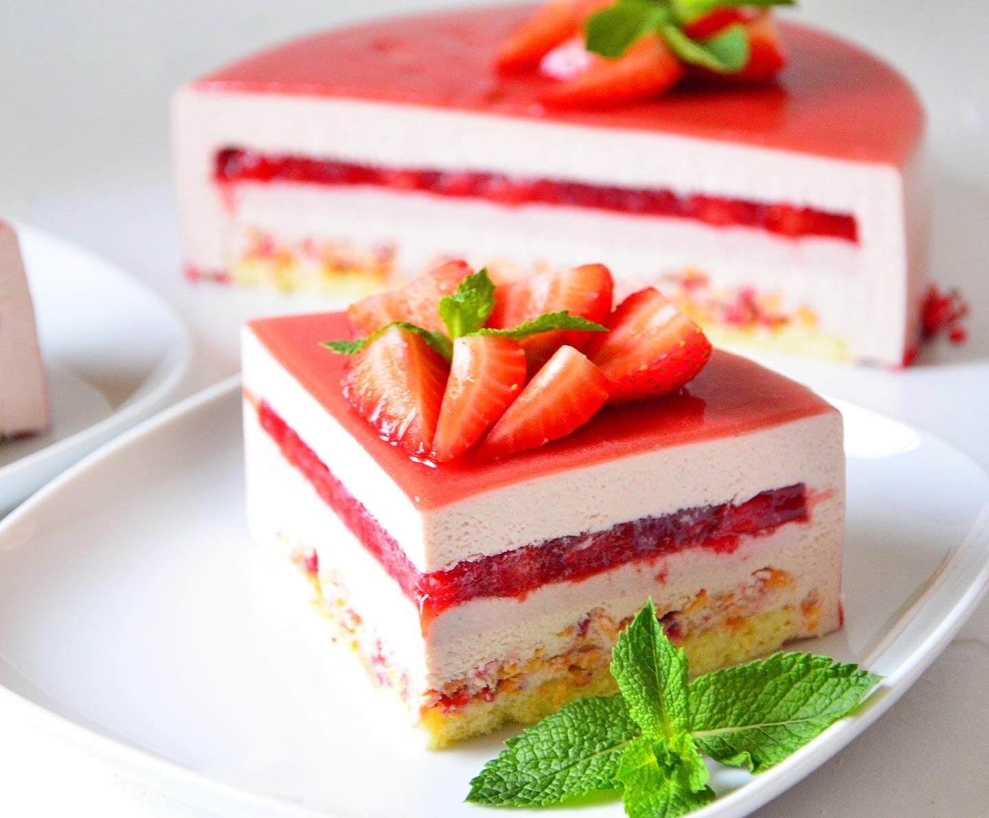 Slice of strawberry mousse cake with red glaze, fresh strawberries and mint on a white plate