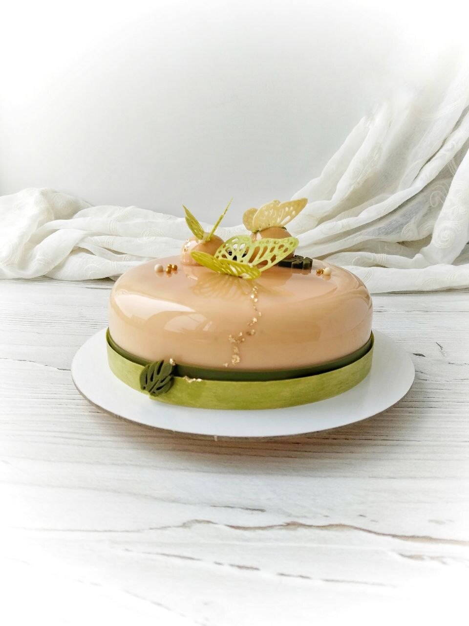 Glazed peach-colored mousse cake with a green band and chocolate butterfly decorations