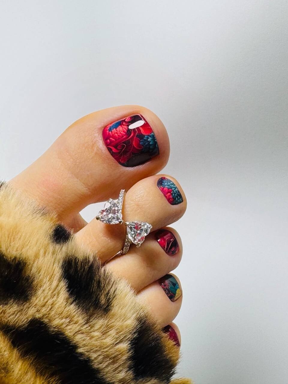 Toes with dark red floral nail art and heart-shaped diamond rings