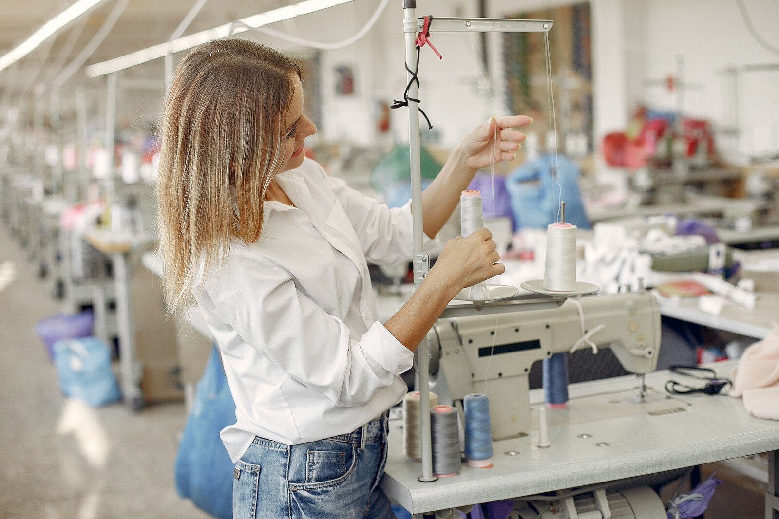 Woman in a white shirt threading an industrial sewing machine