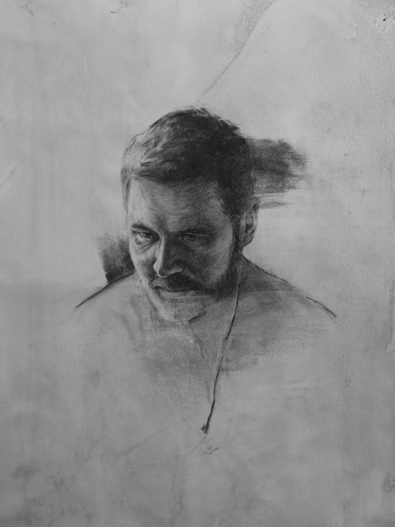 Charcoal portrait sketch of a bearded man looking downward with shoulders lightly outlined