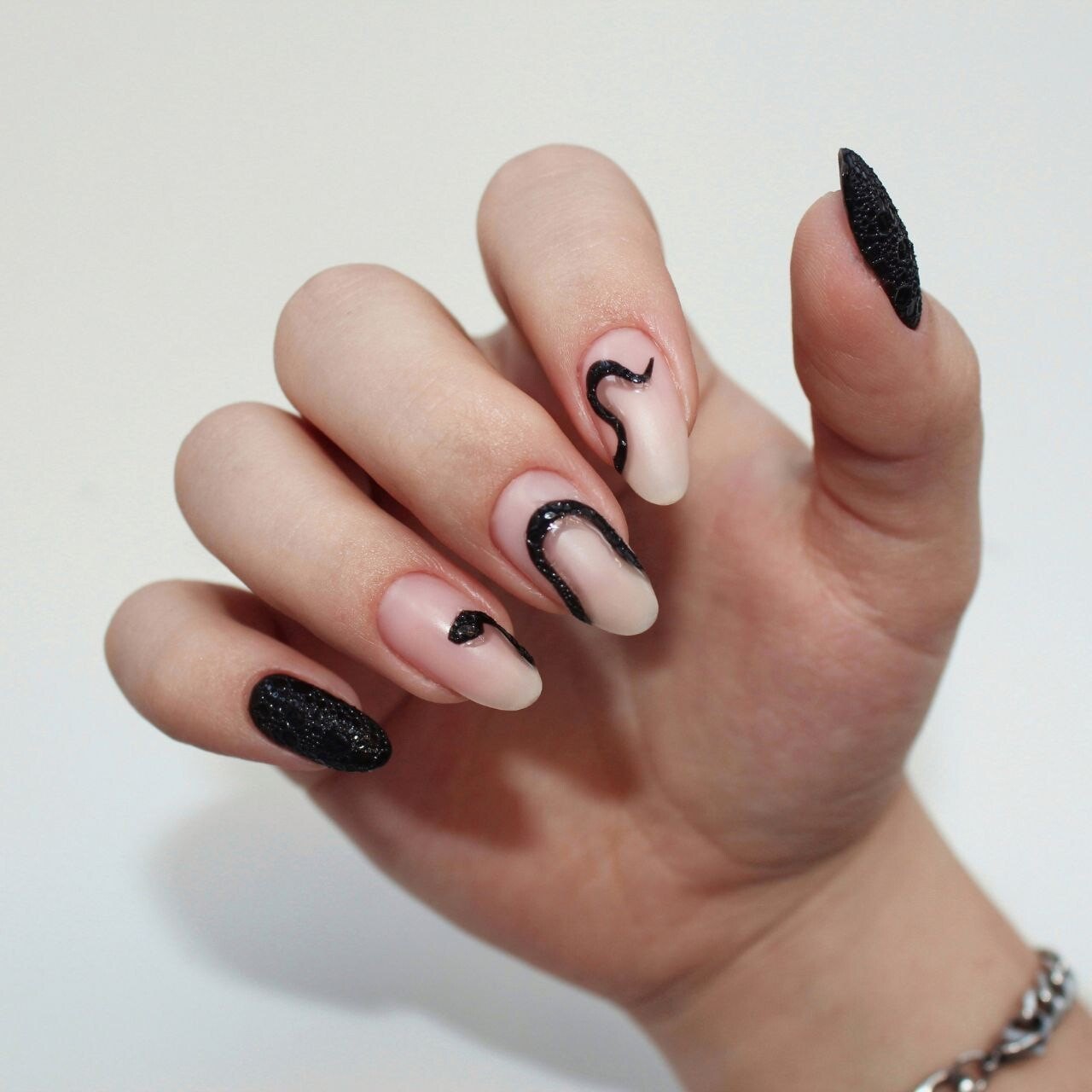 Hand with nude and black nails featuring snake line art and textured black accents