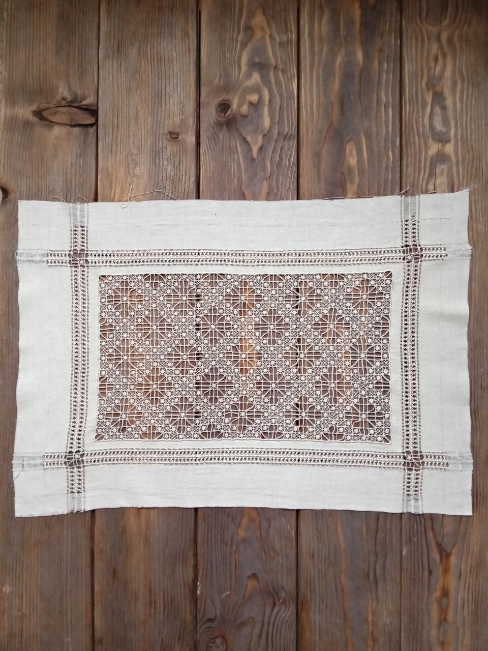 Rectangular linen piece with an openwork lace centre and hemstitched borders on dark wooden planks