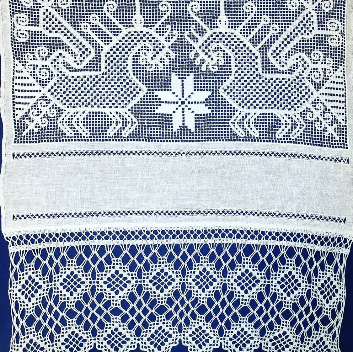 White filet lace and linen towel with stylised bird motifs and a snowflake on a blue background