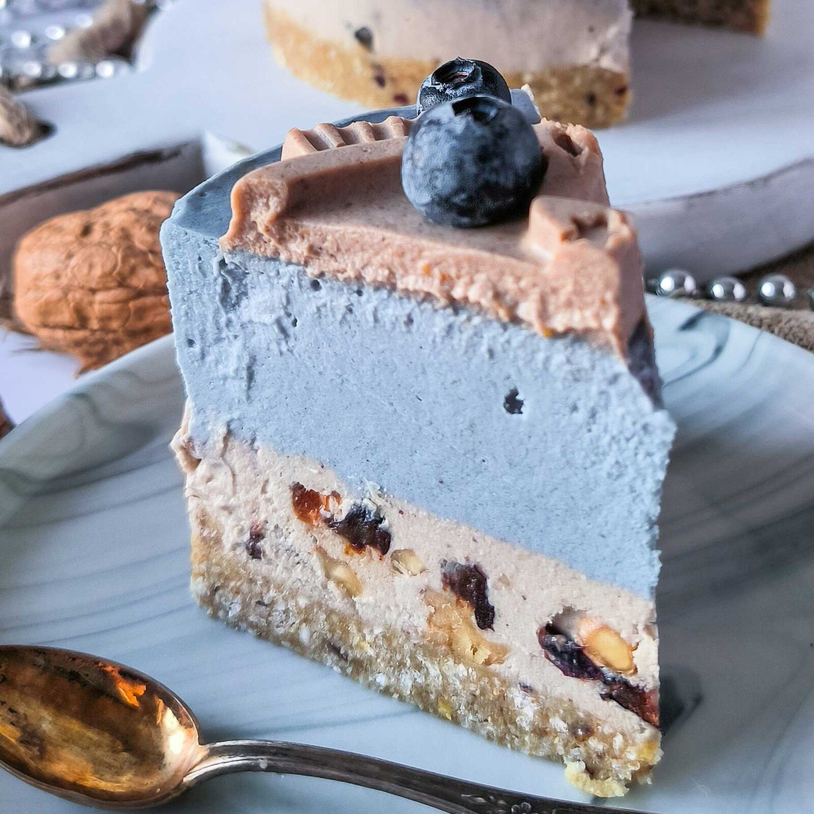 Slice of blue and beige layered raw cake with a blueberry on top and a spoon