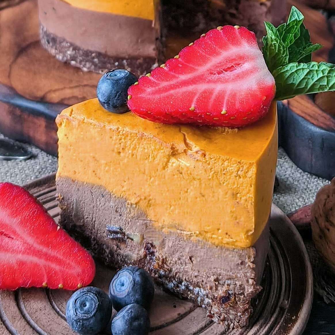 Slice of orange and chocolate raw cake topped with strawberry, blueberry and mint