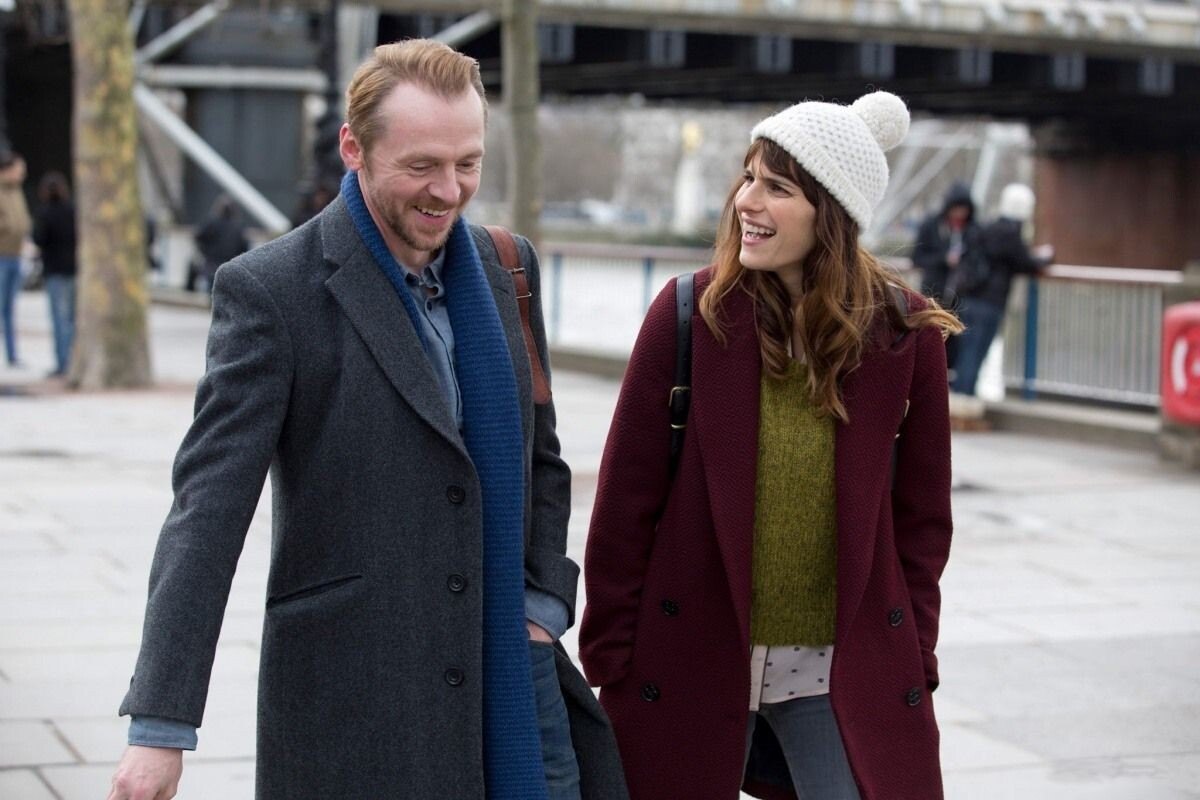 A smiling man and woman in winter coats walking along a riverside promenade