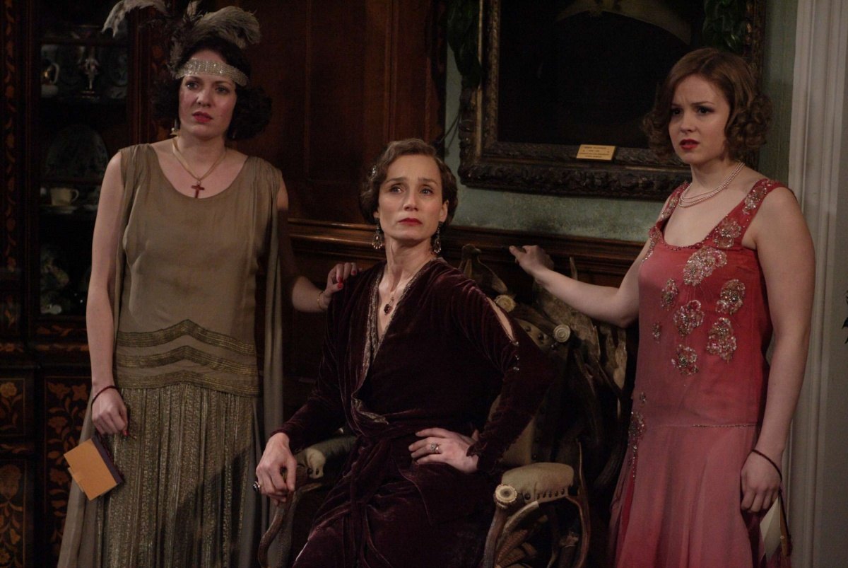 Three women in 1920s style dresses standing in a wood-paneled room looking concerned