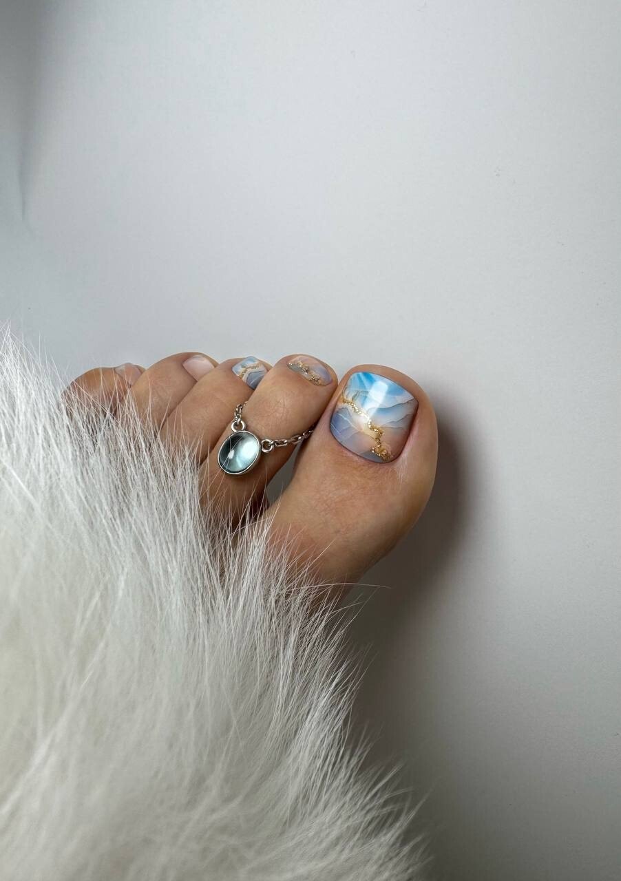 Toes with blue marble nail art and a silver toe ring beside white fur