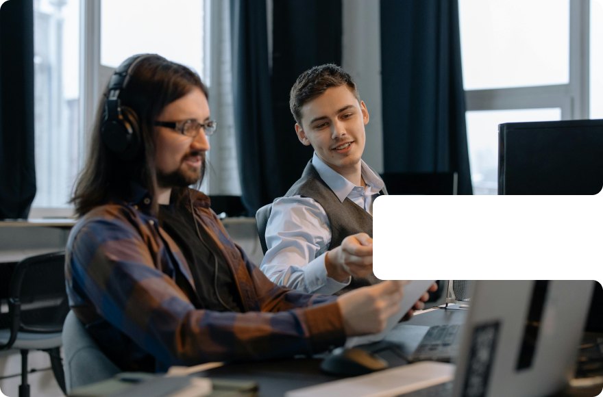 Two colleagues with headphones looking at a paper next to a laptop in an office